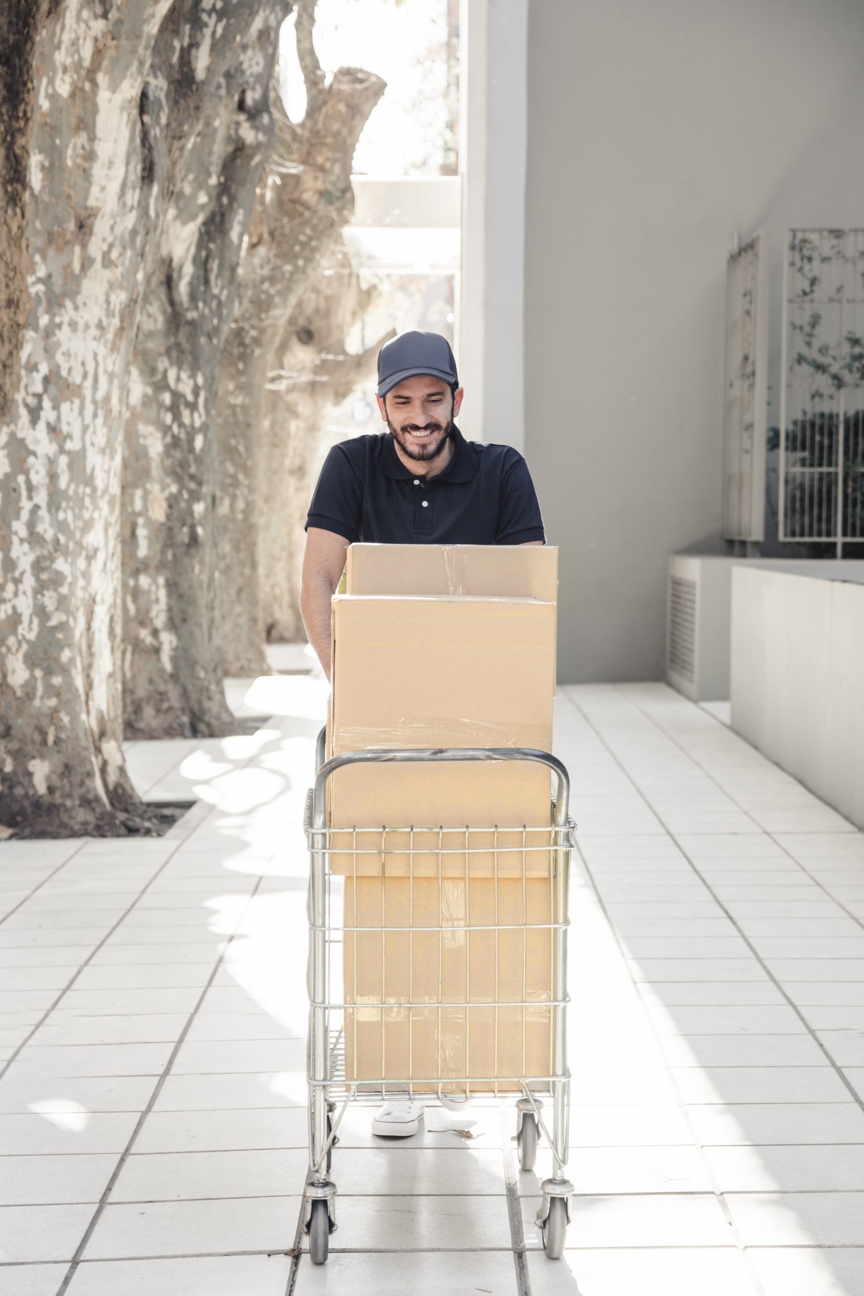 smiling-delivery-man-walking-pavement-with-trolley-full-cardboard-boxes